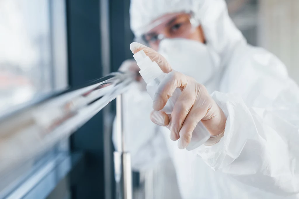 Mensch in Schutzanzug sprüht Geländer ein